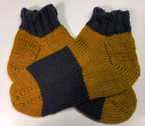 A pair of socks, one on top of the other. The bottom one has the toes pointing right, the top one have them pointing left.
Toe and heel section is in the color curry, midsection and cuffs are dark gray. They are ankle socks.